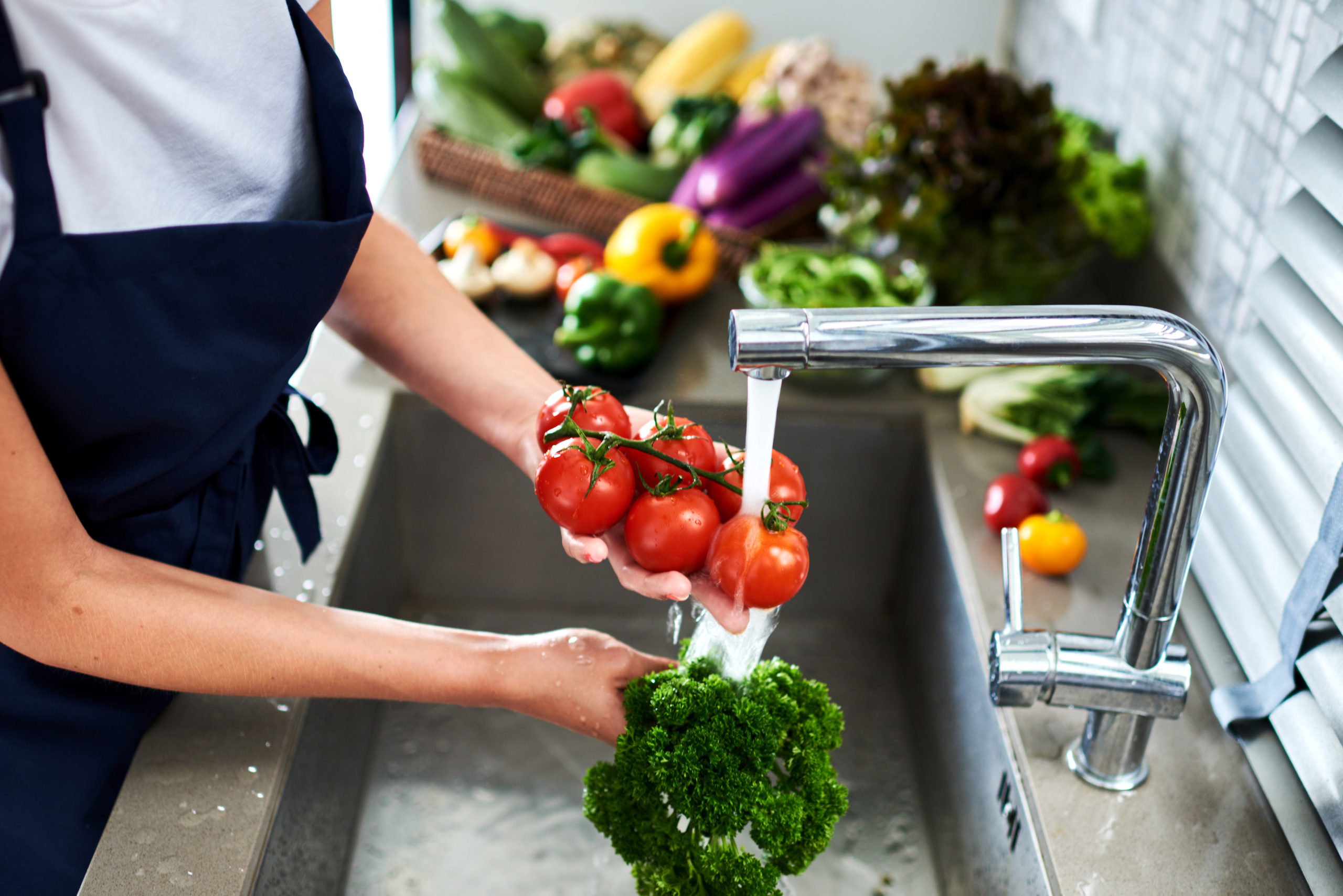 Hands woman  washing vegetables broccoli and tomatoes. Preparation of fresh salad. Fresh vegetables on the worktop near to sink in a modern kitchen interior, healthy food concept. Selective focus.